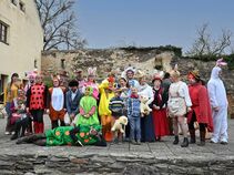 Großes Gruppenbild aller Mitwirkenden in bunten Tier- und Osterkostümen vor der historischen Kulisse von Burg Ranis. Kinder und Erwachsene lachen in die Kamera.