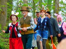 Gruppe fröhlicher Menschen mit Hasenohren und geschminkten Gesichtern bei einem gemeinsamen Osterspaziergang im Wald.