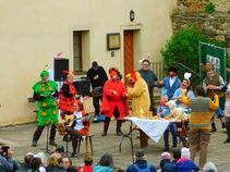 Bühnenaufführung mit vielen verkleideten Darstellerinnen als Tiere und Frühlingsfiguren. Kinder und Erwachsene tanzen und musizieren, ein Publikum schaut zu.