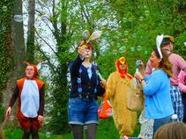 Verkleidete Erwachsene beim Osterspaziergang pusten Seifenblasen, darunter ein Hase, ein Huhn, ein Eichhörnchen und weitere Teilnehmer.
