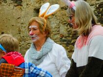 Zwei Frauen mit Hasenohren und bemaltem Gesicht sprechen mit einem Kind in Hasenkostüm. Sie stehen vor einer alten Steinmauer auf dem Burghof.